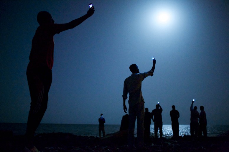 Inmigrantes africanos en la orilla de la ciudad de Yibuti en la noche levantan sus teléfonos en un intento de captar una señal de bajo coste de la vecina Somalia, un tenue vínculo con familiares en el extranjero. Autor: John Stanmeyer