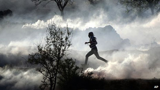 Manifestante palestino corre en medio de botellas de gas lacrimógeno. [Fuente: ABC Local]