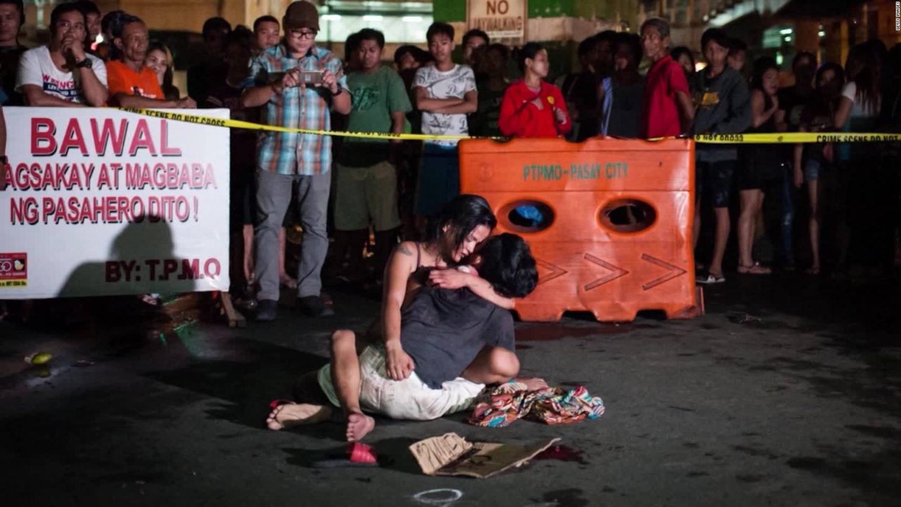 Una mujer abraza a su pareja asesinada por un grupo de vigilantes al lado de un cartel que reza: "vendedor de droga". Imagen: CNN / Getty Images.